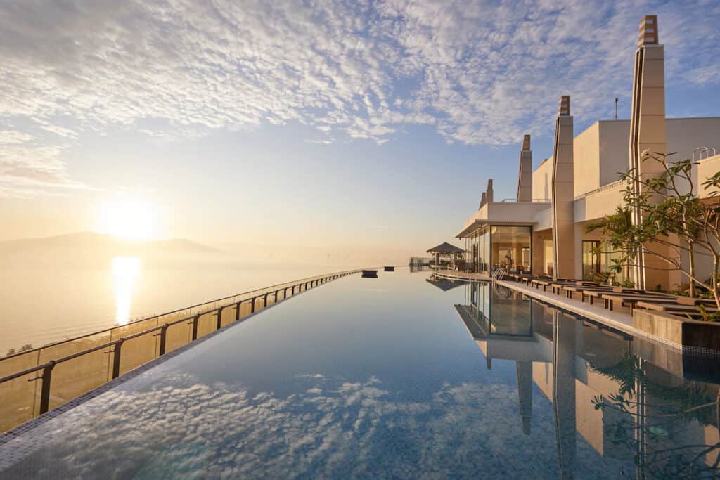 Sunrise view from an infinity pool at Mikazuki Japanese Spa and Resort, with the calm waters mirroring the sky and overlooking a distant mountain silhouette